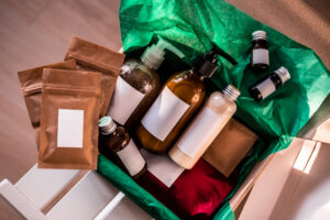 A box filled with various cosmetic items in bottles, pouches, and bags, each with a white label attached, prepared for a custom design to be affixed