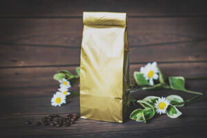 A coffee bag with no label design with a handful of coffee beans and some daisies on the table with it